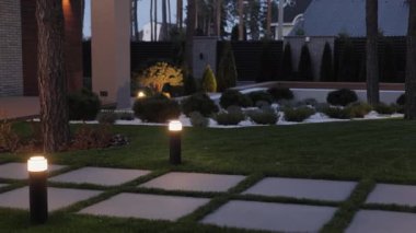 Geceleri bahçe düzenleme işi. Fenerler yolu yumuşak ışıkla aydınlatır. Çimlerin üzerindeki sokak lambaları. Ilık parıltı yemyeşil yeşilliği vurguluyor ve rahatlatıcı bir atmosfer yaratıyor. Yüksek