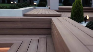 Akşam evin yanındaki bahçenin yanındaki ahşap terasın yakın çekimi. Dış görünüş ve tasarım. Aydınlatılmış ahşap terası olan akşam rahatlama alanı. Yüksek kalite 4k görüntü