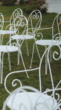 Dikey video. Düğün törenindeki misafirler için beyaz metal sandalyeler. Açık havada düğün töreni. Dekor, çimenlikteki düğün töreni için sandalyeler. Düğün dekoru. Yüksek kalite 4k görüntü