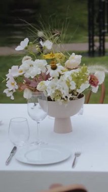 Dışarıdaki masada bir vazo çiçek. Düğün ya da etkinlikte üzerinde çiçekler ve mumlar olan masa. Düğün dekorasyonu, dekore edilmiş masalar, açık masa seti. Verticsl video. Yüksek kalite 4k görüntü