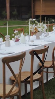 Açık hava düğünü için çiçek sehpası. Düğün dekoru, cam, çiçekler, mumlar. Akşam yemeği için zarif ve büyüleyici bir ortam. Tahta sandalyeler, düğün yemeği. Dikey video. Yüksek kalite 4k görüntü