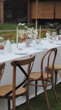 Dikey video. Düğün masası ayarı. Düğün ya da açık hava partisi için çiçek sehpası. Sandalyeler, cam, çiçekler, mumlar. Zarif ve büyüleyici bir akşam yemeği. Yüksek kalite 4k görüntü