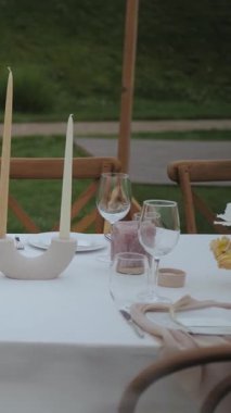 Açık havada kır çiçekleri, mumlar, tabaklar, düğün veya etkinlikte ahşap sandalyeler, arka planda yeşil çimenler, yavaş çekim. Dikey video. Yüksek kalite 4k görüntü