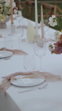 Süslü düğün masası. Açık hava ziyafeti, çiçekli masa, mumlar, sandalyeler, küçük rahat bir düğün partisinde beyaz tabaklar, yiyecek yok. Dikey video. Yüksek kalite 4k görüntü