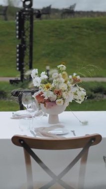 Düğün dekorasyonu, dekore edilmiş masalar, açık hava masaları. Çiçek aranjmanı açık havada bir düğün masasında. Bir düğün ya da etkinlikte düğün dekoru. Cam, çiçek, mum. Dikey video. Yüksek kalite 4k