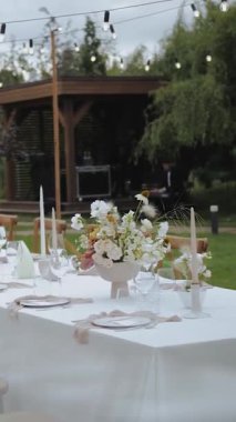 Süslü yemek masasında vazo ve bir buket pastel taze çiçek var. Açık hava düğün yemeği. Yemek yok. Düğün etkinliği ya da fonksiyon için çiçek aranjmanı. Yüksek kalite 4k görüntü
