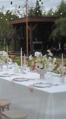 Düğün dekoru, akşam yemeği. Vazo ve bir buket çiçekle süslenmiş yemek masası. Açık hava etkinliği. Yemek yok. Düğün etkinliği ya da fonksiyon için çiçek aranjmanı. Dikey video. Yüksek