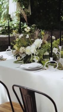 Bir restoranda düğün masası dekoru. Taze yeşil arka planda mumlarla güzel ve zarif bir çiçek masası. Yüksek kalite 4k görüntü