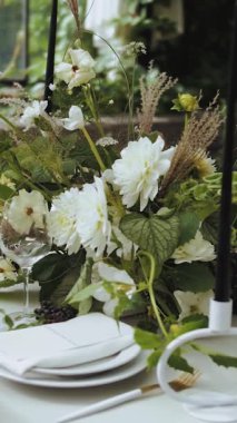 Tabaklar, mumlar ve çiçeklerle süslenmiş bir masa. Yemek masasına çiçeklerle servis yapmak. Şenlikli bir akşam yemeği ya da parti, içeride. Düğün günü. Dikey video. Yüksek kalite 4k görüntü