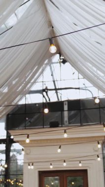 Dikey video. Restoranın tavanında ampuller, barda retro çelenkler, düğün için güzel dekorasyon, odağını kaybetmiş çerçeve, yavaş çekim. Yüksek kalite 4k görüntü