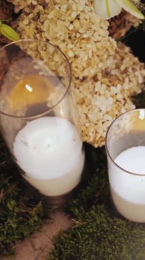 Yakından mum yakıyorum. Yakıcı mumları olan güzel bir çiçek dekoru. Camdaki mumlar yeşil yosun üzerinde duruyor. Pastel renklerde şenlikli dekor, yavaş çekim. Dikey video. Yüksek kalite 4k görüntü