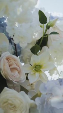 Dikey video. Mavi gökyüzüne karşı düğün kemerinde çiçekler. Beyaz ve mavi çiçeklerle süslenmiş kemer, güller, kasımpatılar ve ortancalar. Düğün kemeri töreni. Yüksek kalite 4k görüntü