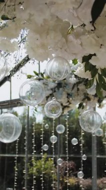 Yeni evlilerin düğün masasının üstündeki bir restoranda çiçek aranjmanı. Beyaz çiçekli çadır, süslü ziyafet salonu. Masanın üstündeki çiçek aranjmanı. Dikey video. Yüksek