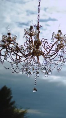 Açık havada kristal avize, masanın üstünde asılı düğün dekoru arka planda bulutlu gökyüzü, yakın plan. Dikey video. Yüksek kalite 4k görüntü