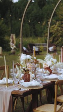 Dikey video. Açık hava düğün resepsiyonu, mumlar ve kurutulmuş masalar ve boho düğünü için pastel çiçekler, tabaklar ve bardaklar, insan yok. Yüksek kalite 4k görüntü