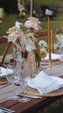 Dikey video. Düğün masasında mumlar, kurutulmuş çiçekler ve pastel çiçekler. Açık hava partisi, tabak ve bardaklar, insan ya da yiyecek yok. Yüksek kalite 4k görüntü