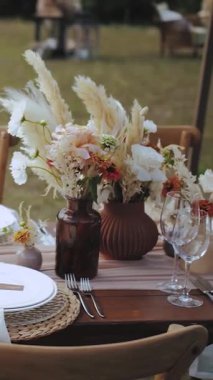 Düğün dekoru, şenlikli yemek ya da parti. Açık hava şenlikli bir akşam yemeği için çok güzel dekore edilmiş bir masa. Boho düğünü, beyaz tabaklar, tahta bir masada gözlük. Yüksek kalite 4k görüntü