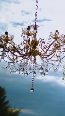 Dikey video. Düğün masasının üstünde klasik kristal avize arka planda bulutlu gökyüzü, orta çekim, yavaş çekim. Düğün dekoru. Yüksek kalite 4k görüntü