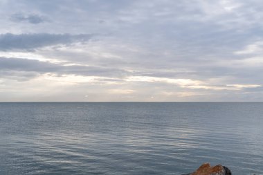 Sakin bir deniz manzarası, yumuşak ışığı yansıtan sakin bir okyanusla alacakaranlığı yakalar. Geniş bulutlu bir gökyüzünün altında kayalık bir sahile doğru yumuşak dalgalar süzülür..