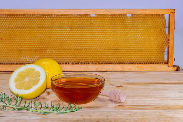 İçinde bal, şeker kutusu, biberiye filizi ve arka planda gerçek bir bal peteği olan ahşap üzerine bir buçuk limon. Metin için boşluk