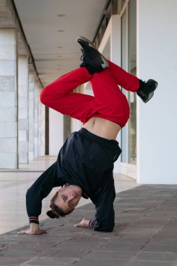 Siyah kazaklı ve kırmızı pantolonlu bir adam break dans yapıyor. Atletizm ve maharet kavramı. Adam baş aşağı dururken elleri üzerinde denge kurabiliyor..