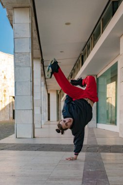 Siyah kazaklı ve kırmızı pantolonlu genç bir adam kaldırımda dans ediyor. Atletizm ve el becerisi kavramı, bir yandan baş aşağı durarak dengeyi koruyabilmesi gibi..