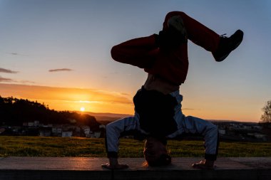 Arka planda, arka planda şehir olan bir günbatımının önünde break dans yapan genç bir adamın yansıması. Huzurlu ve huzurlu bir ortamda bir insan olarak.
