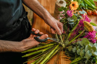 Çiçekçi dükkanında çiçek buketi buketinin etrafına kurdele bağlar ve çiçek keser.