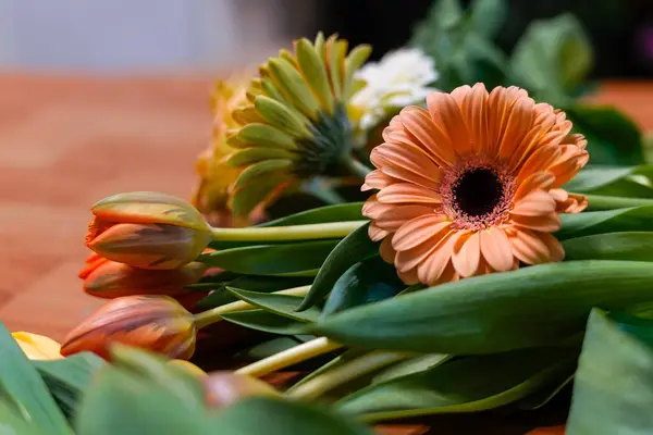 Canlı turuncu gerbera ve laleler ahşap bir masanın üzerine uzanmış güzel bir çiçek aranjmanı yaratıyorlar.