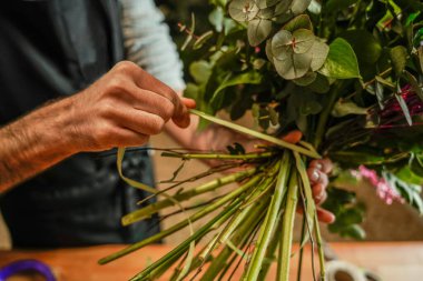 Çiçek saplarının etrafına kurdele bağlayan, okaliptüs ve renkli çiçeklerle güzel bir buket yapan bir çiçekçi.