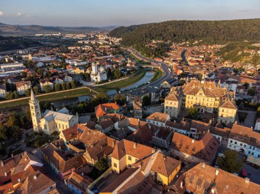 Günbatımında kiliseler, eski binalar ve dolambaçlı bir nehrin yer aldığı tarihi bir Romanya kenti olan Sighisoara 'nın insansız hava aracı görüntüsü. Turizm ve mimari temalar için mükemmel.
