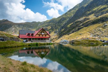 Transfagarasan yolundan geçen ünlü Balea Gölü 'nün panoramik manzarası, otelin yansıması ve sudaki Carpathian Dağları. Romanya. Yaz Sürümü