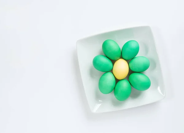 Yellow Egg surrounded by Green eggs on White Plate and Background