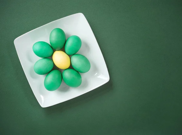 Green Eggs Surrounding Yellow Egg on White Plate on Green Background