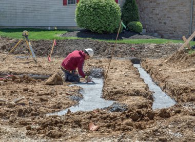 Dayton, Ohio - 25 Nisan 2024: Masonluk inşaat işçisi yeni konut geliştirme temelinde betonu yumuşatıyor.