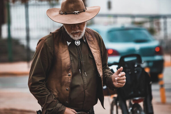 Man in a cowboy hat and vest standing on a sidewalk