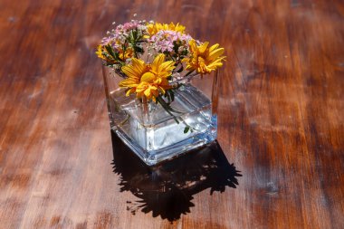 Tahta bir masada cam bir kavanozda güzel sarı kasımpatı çiçekleri.