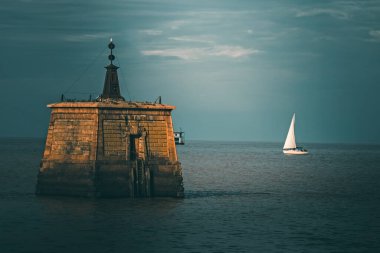 Limandaki deniz fenerinin gündüz görüntüsü bulutlu gökyüzünün altında 