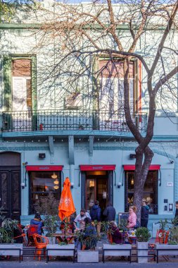 İnsanlar sokakta açık bir kafede oturuyorlar. 