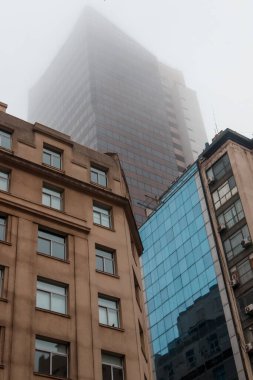 Uzun, modern gökdelen kalın sisin içinde kayboluyor.