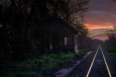 Terk edilmiş tren istasyonu, gün batımının parlayan raylarının yanında.