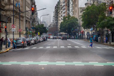 Park halindeki arabaları ve yaya geçidi olan kalabalık bir şehir caddesi.