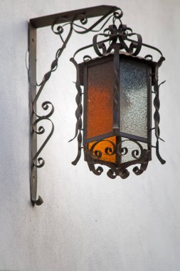 Beyaz duvara asılı süslü metal fener.