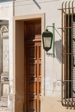 Güneş ışığıyla aydınlatılmış ahşap kapı, klasik fener ve pencerenin yanında.