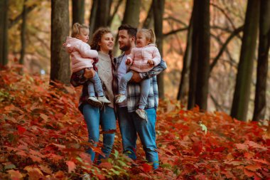Bir aile, sonbaharın ortasında iki küçük ikiz kız kardeşle yürüyor.; 