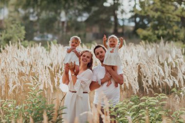 Bir aile doğanın ortasında iki çocuk, ikiz kız kardeş ile yürür; ebeveynler küçük çocuklarla oynar ve onları ellerinin başının üstünde tutarlar; aile hafif giysiler giyer.