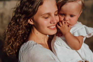 Bir aile doğanın ortasında iki çocuk, ikiz kız kardeş, kollarında kızı olan bir anne ve açık renk giysiler içinde yürür.