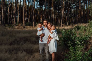 Bir aile doğanın ortasında iki çocuk ve ikiz kız kardeşle yürür.;