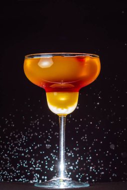 Siyah bir duvarın arkasında cam bir kapta alkollü kokteyl ve su damlaları.