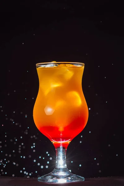 alcoholic cocktail in a glass container on the background of a black wall and drops of water